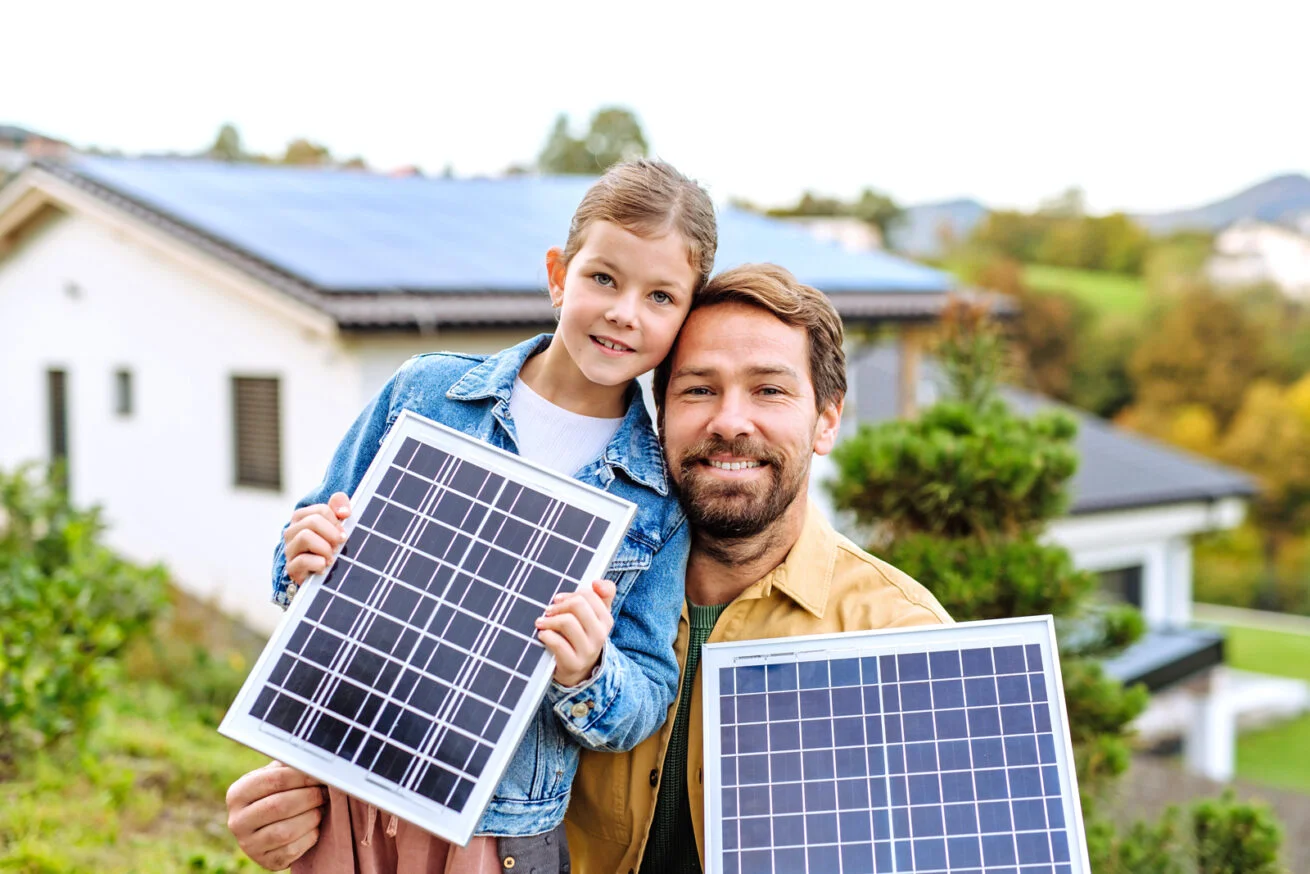 Vater und Tochter mit Solarmodulen vor ihrem Haus – KfW Förderung Köln.