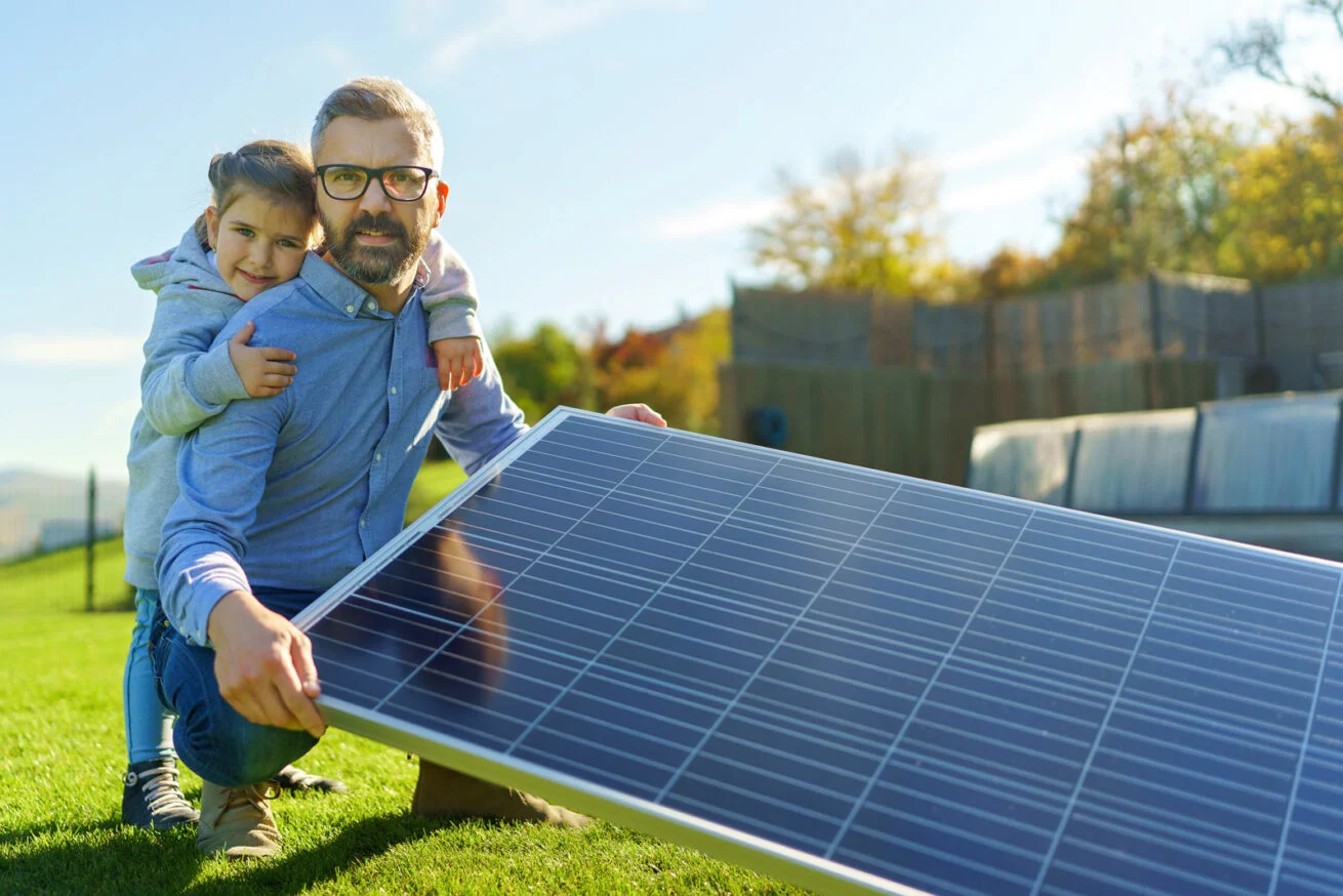 Vater mit Tochter und Solarmodul im Garten – Investitionsförderung Solaranlagen Köln.